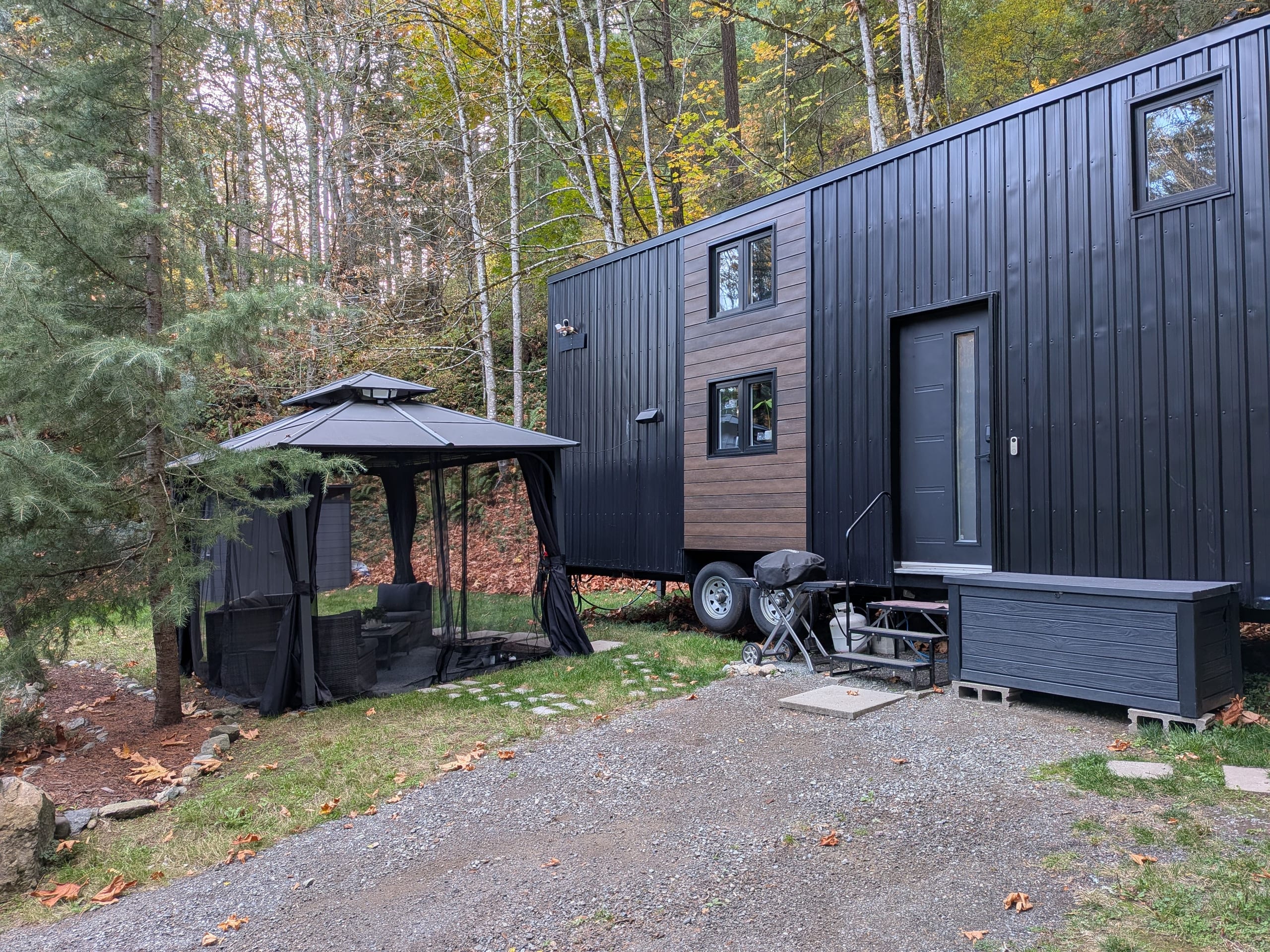 Side view of the steel-clad tiny house beside the screened gazebo and wooded yard