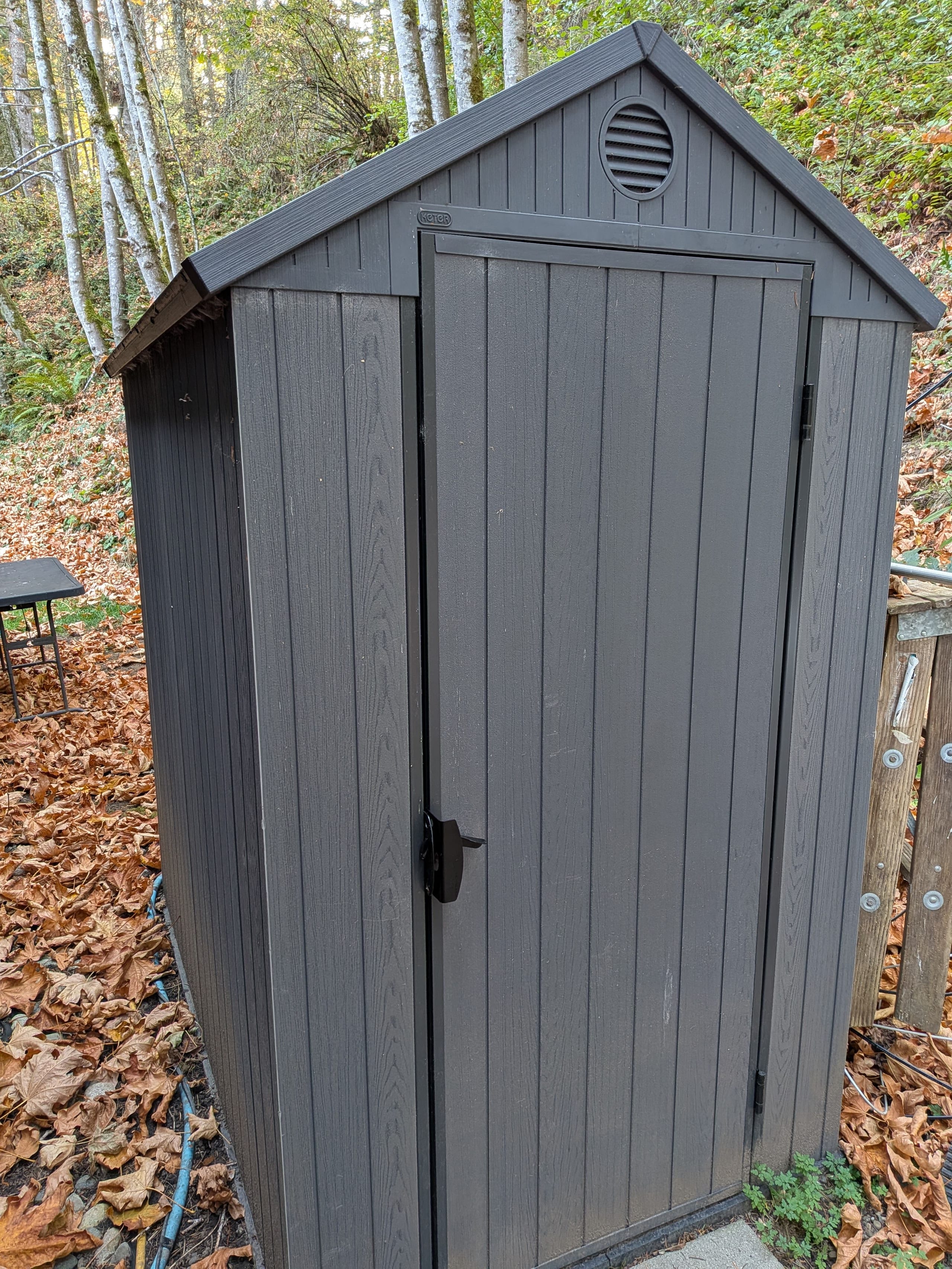 Grey storage shed among trees at the edge of the yard